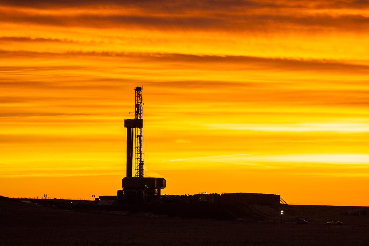 Silhouette of a drilling rig against an orange sunrise sky in southeastern Wyoming